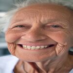 A realistic photo of an elderly Spanish person smiling, showing natural-looking dental implants, in a modern dental clinic with soft lighting.