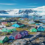 Aerial view of a small Greenlandic settlement with colorful houses on a rocky coast, surrounded by icebergs and a glacier in the background, under a clear blue sky, photorealistic style.