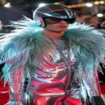 Sam Smith at the Met Gala 2026 wearing a futuristic silver latex suit with neon ostrich feathers and a holographic helmet, standing on the red carpet with a confident pose, surrounded by photographers