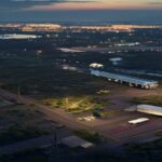 A photorealistic aerial view of Newark Liberty International Airport at dusk, with a damaged light pole near the runway and a delivery truck with a dented roof, surrounded by industrial areas and wetl
