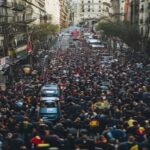 A crowded street in Barcelona with thousands of FC Barcelona fans celebrating, traffic jam, metro station closed sign, police officers managing crowd, urban chaos, photorealistic, wide angle shot.