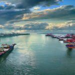 Aerial view of the Zárate port on the Paraná River, Argentina, with cargo ships and container cranes, under a cloudy sky, photorealistic style.