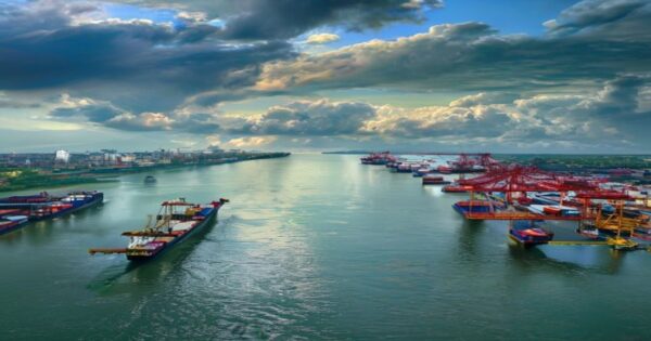 Aerial view of the Zárate port on the Paraná River, Argentina, with cargo ships and container cranes, under a cloudy sky, photorealistic style.