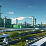 A photorealistic wide shot of a large green hydrogen production facility in Spain, with rows of electrolyzers and solar panels in the background under a clear blue sky. The facility is modern, with wh