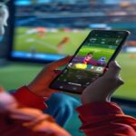 A realistic photo of a person using a smartphone app with a 'Cash Out' button highlighted, showing a live sports match in the background, modern interface, bright colors, no text or logos.