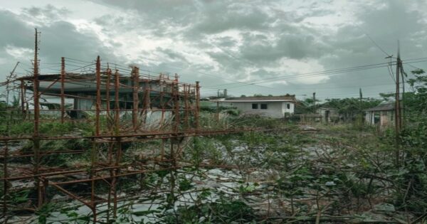 Sobrecostos en hospitales hondureños: corrupción y desigualdad 2 A photorealistic image of an unfinished hospital construction site in a rural area of Honduras, with rusted scaffolding and overgrown weeds, symbolizing abandoned projects and cost overruns. The backg