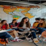 A photo-realistic image of a diverse group of young people from Latin America and Spain (including indigenous, afro-descendant, and urban youth) sitting in a circle in a bright, modern meeting room. T