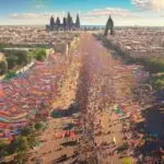Aerial photorealistic view of a massive LGBTQ+ Pride demonstration in Barcelona, sunny day, colorful flags, crowd filling the wide Gran Via avenue, Sagrada Familia in background