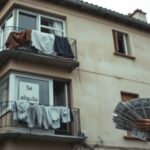 A realistic photo of a modest apartment building in Galicia, Spain, with a sign reading 'Se alquila' in the window. The facade shows wear and aging, with laundry hanging from balconies. In the foregro
