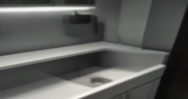 Detectores de fugas: el descuento del seguro que puede penalizarte 2 A modern smart water leak detector installed on a pipe under a kitchen sink, with a glowing status light and a smartphone notification floating nearby, realistic home setting, soft lighting, no text.